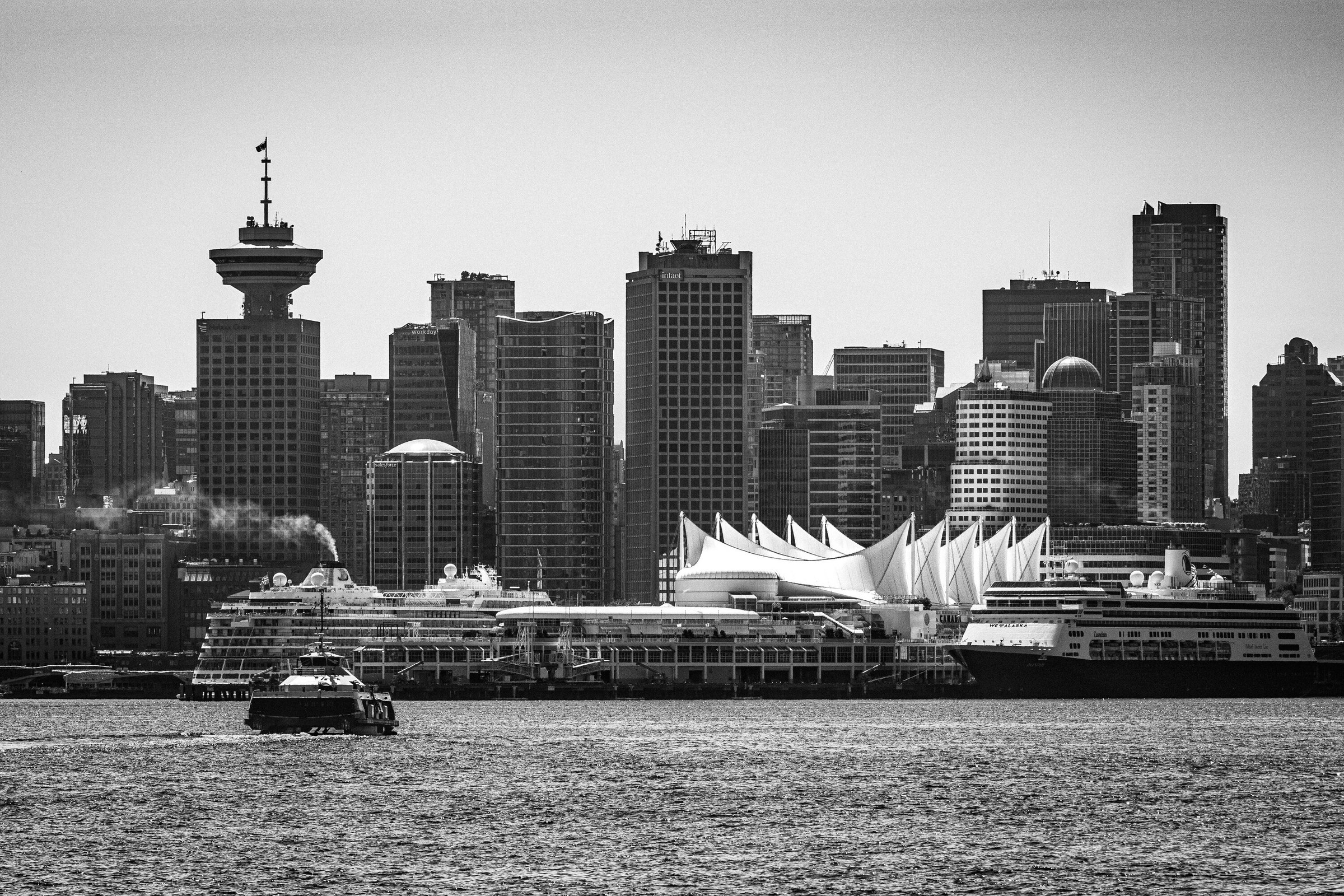 Black and white view of the downtown Vancouver waterfront, Canada Place sails and a moored cruise ship below a wall of towers.