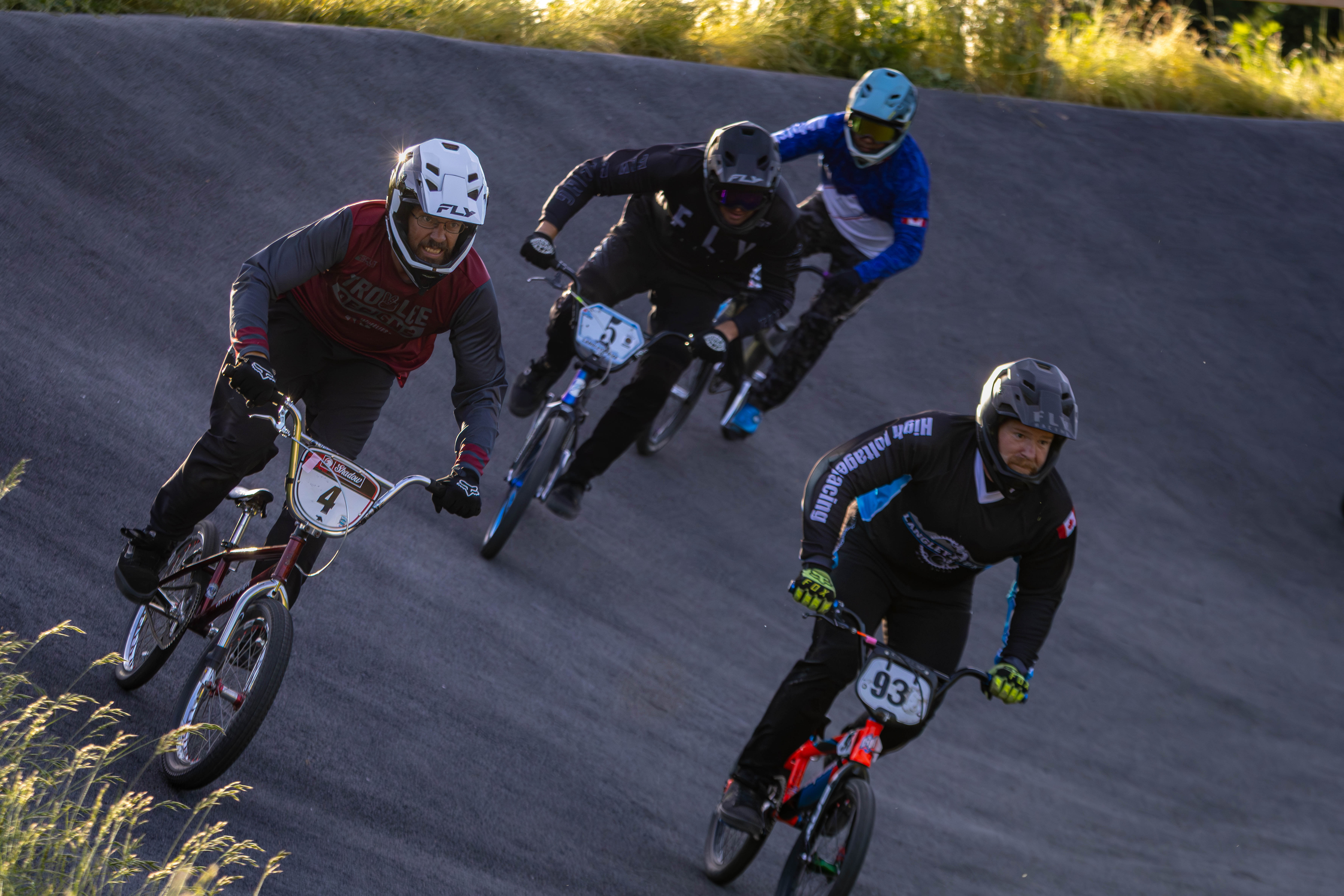 BMX racers carve through a banked corner in golden light
